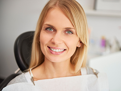 Blonde woman smiling in dental chair after successful dental treatment at North County Cosmetic and Implant Dentistry in Vista, CA
